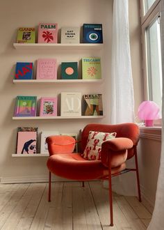 an orange chair sitting in front of a window next to a book shelf filled with books