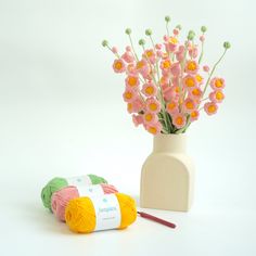 a white vase with pink flowers next to a crochet kit and knitting needles