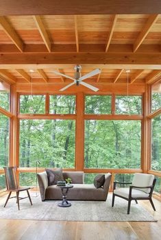 a living room filled with furniture and windows covered in wooden beams, surrounded by trees