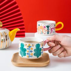 a person is holding a cup in front of two teapots on a table