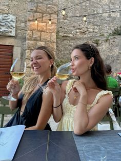 two women sitting at an outdoor table drinking wine