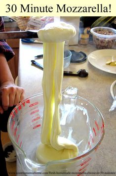 a person pouring cheese into a glass bowl