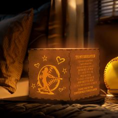 an illuminated baseball sits on a bed next to a lamp that reads, i love my daughter