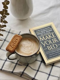 a cup of coffee and a cookie on a table next to a book about make your bed