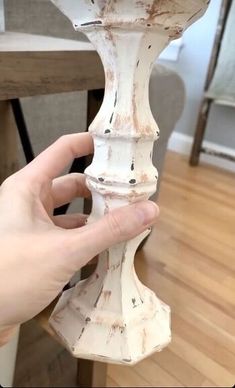 a hand holding a white vase on top of a wooden table