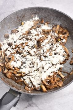 a pan filled with mushrooms and cheese on top of a marble countertop next to a spatula