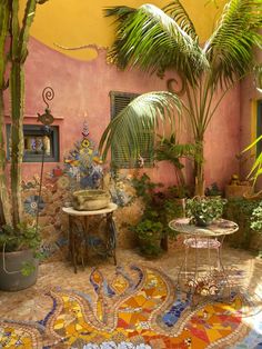 an outdoor area with potted plants, tables and rugs on the ground in front of a pink wall