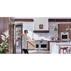 a woman is opening the door to her kitchen with an oven and refrigerator in it