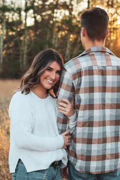 a man and woman standing next to each other in front of tall grass with trees behind them