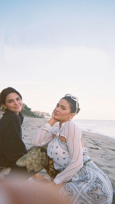 two women sitting on the beach next to each other