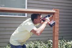 a man using a power drill to attach a wooden fence post in front of a house