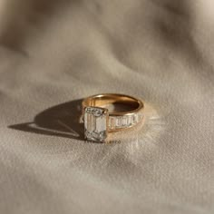 a gold ring with a baguette cut diamond in the center on a white cloth