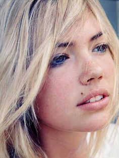 a close up of a person with long blonde hair and blue eyeliners, wearing a white shirt