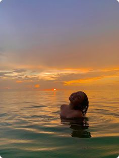 a woman floating in the ocean at sunset with her head above the water's surface