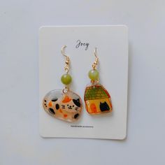 a pair of earrings with cats and a house on them sitting on top of a card