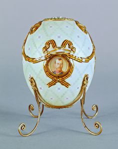 an ornate white and gold egg with a portrait on the front, sitting on a stand