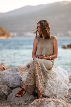 a woman sitting on top of a rock next to the ocean holding a cell phone