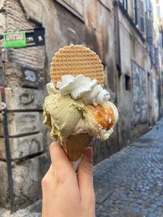 a hand holding up an ice cream cone with waffles and whipped cream on top