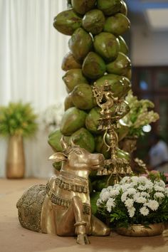 an arrangement of fruit and flowers on a table in front of a large stack of bananas