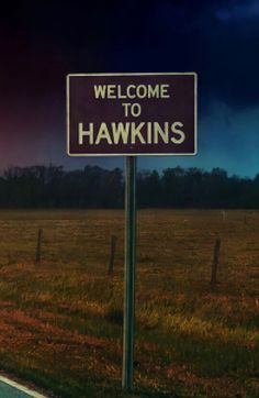 a welcome to hawks sign in the middle of a field with dark clouds behind it