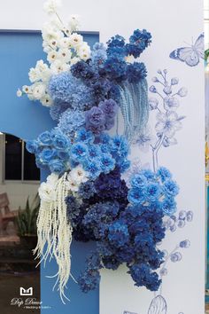 blue and white flowers hanging on the side of a building next to a butterfly mural