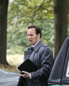 a man in a suit and tie standing next to a car holding a binder