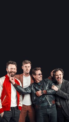 four men are posing together in front of a black background and one is wearing a red jacket