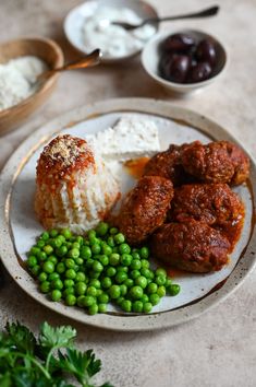 a white plate topped with meatballs, rice and peas next to bowls of sauce