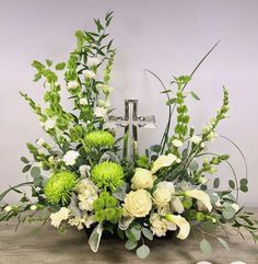 an arrangement of flowers and greenery in a basket on a table with a cross