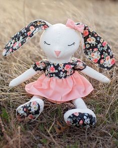 a stuffed rabbit in a pink dress sitting on the ground with grass and flowers around it