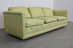 a green couch sitting on top of a cement floor next to a white wall in a room