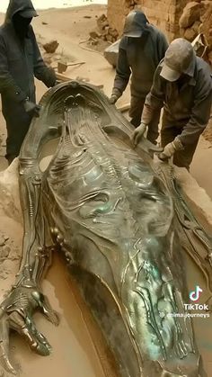 two men are working on a large metal object in the sand, with another man standing next to it