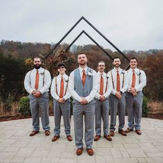 a group of men standing next to each other in front of a metal structure with trees behind them