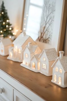 three small white houses sitting on top of a wooden table next to a christmas tree