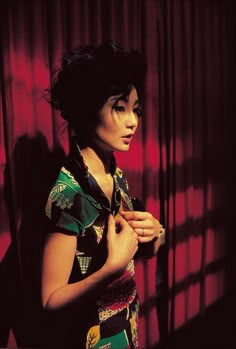 a woman standing in front of a red curtain with her hands clasped to her chest