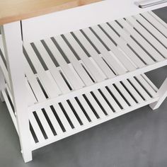 a white bench with wooden slats on the top and bottom, sitting next to a table