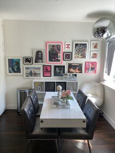 a white table with black chairs and pictures on the wall behind it in a dining room