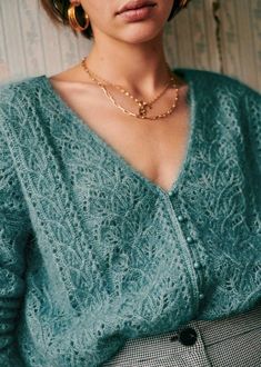 a woman wearing a green sweater and gold hoop earrings is posing for the camera with her hand on her hip