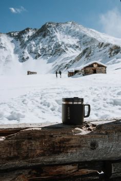 a coffee cup sitting on top of a wooden table next to a snow covered mountain