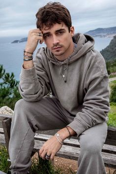 a man sitting on top of a wooden bench next to the ocean with his hand in his ear