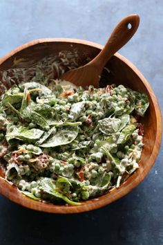 a wooden bowl filled with spinach salad on top of a blue countertop next to a wooden spoon