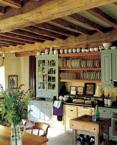 an old fashioned kitchen with green cabinets and white dishes on the counter top, along with a wooden dining room table