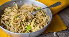 a bowl filled with noodles and vegetables on top of a wooden table next to a yellow napkin