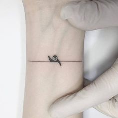 a small tattoo on the wrist with a bird sitting on a wire attached to it