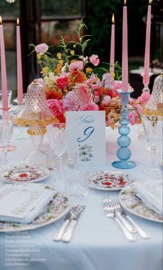 the table is set with pink flowers, candles and place settings for two people to sit at