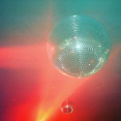 a disco ball hanging from the ceiling in front of red and green light shining down on it