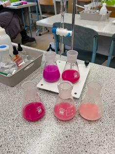 four flasks filled with pink and purple liquid sitting on a counter in a lab