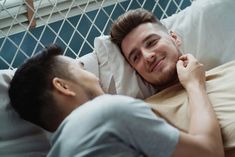 a man laying in bed next to another man who is holding his hand on the pillow