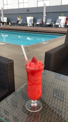 a red drink sitting on top of a table next to a swimming pool