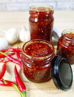 two jars filled with chili sauce sitting on top of a table next to garlic and peppers